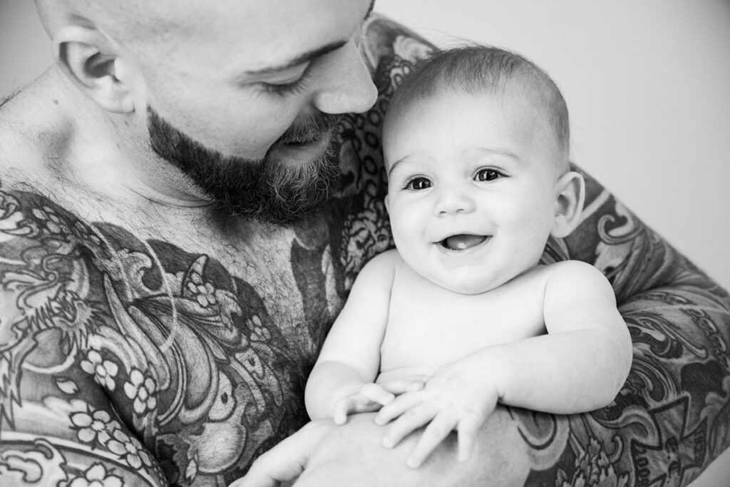 lachendes baby bei seinem tätowierten papa auf dem arm